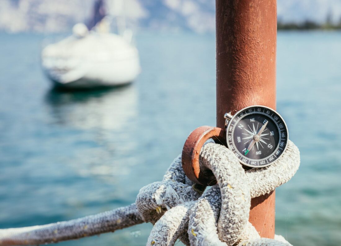 Kompass am Tau eines Steges, Boot im Hintergrund, Navigation